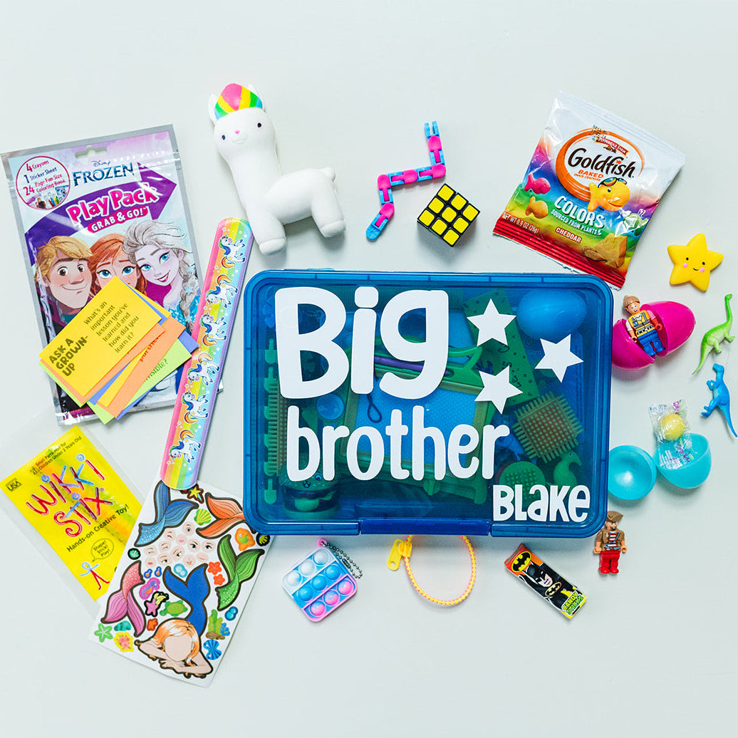 A variety of children's toys and activities are displayed, including coloring books, stickers, mini figures, and fidget toys, with a large blue box in the center labeled 'Big brother' with the name 'Blake' on it.