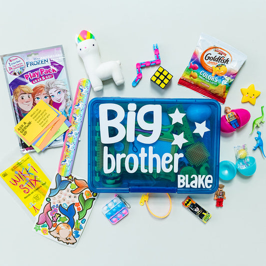 A variety of children's toys and activities are displayed, including coloring books, stickers, mini figures, and fidget toys, with a large blue box in the center labeled 'Big brother' with the name 'Blake' on it.