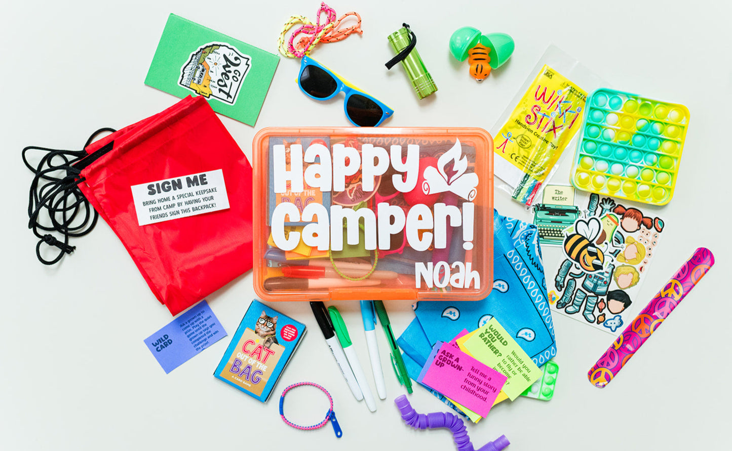 Assorted children's toys and items including a cinch-string backpack, permanent markers, a card game, sunglasses, a fidget pop tube, zipper and rope tie bracelets, a bendy snake, a slap bracelet, activity cards, a mochi squishy, a notebook with stickers, a mini pop it keychain, and a colorful bandana.