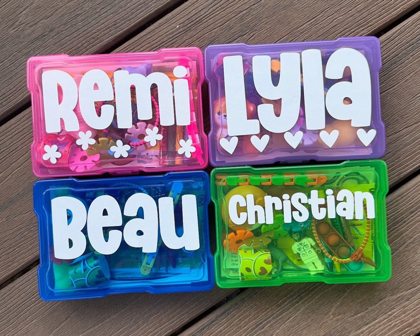 Four colorful name containers with names 'Remi', 'Lyla', 'Beau', and 'Christian' on a wooden surface.