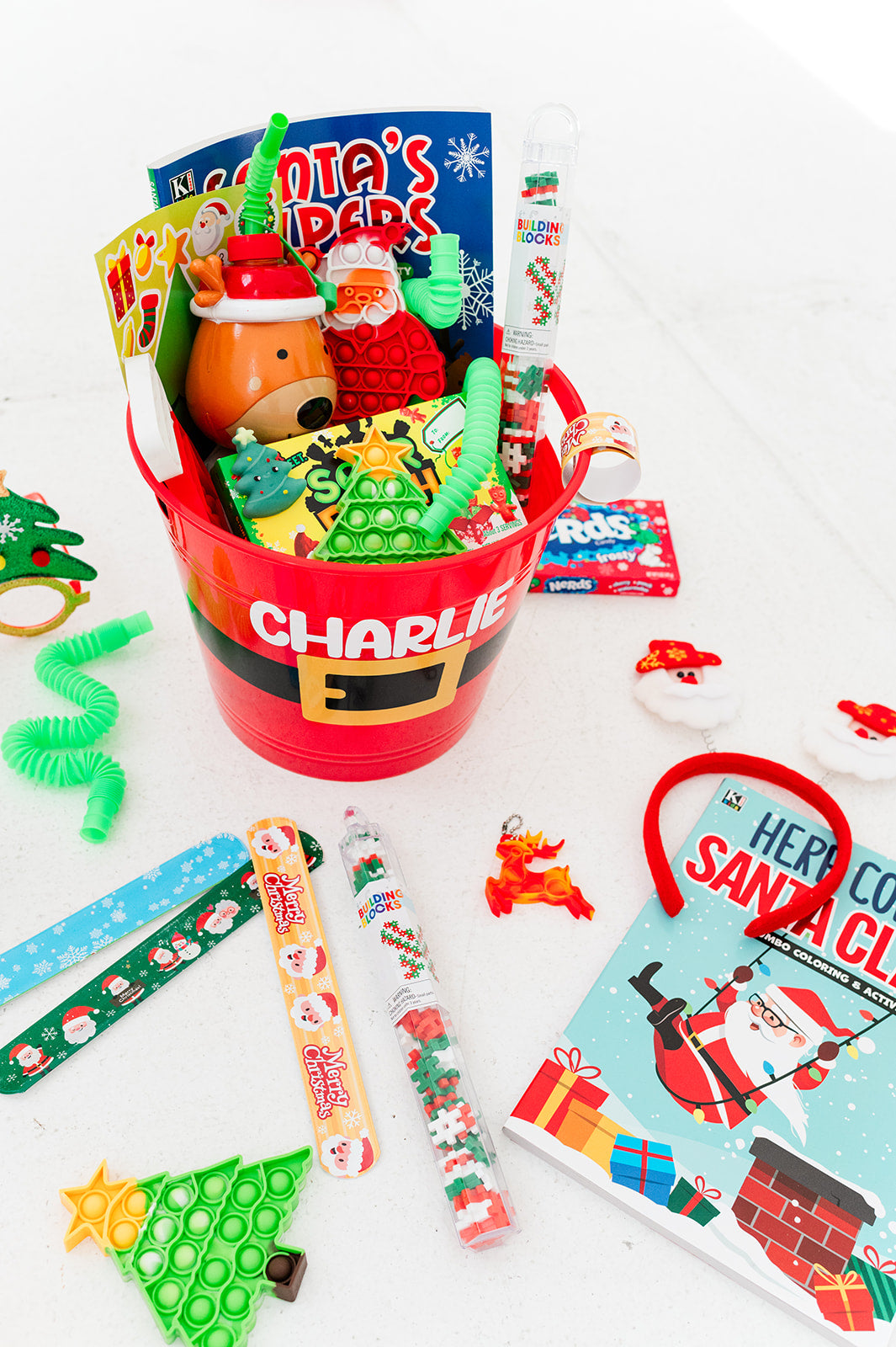 Gift basket with various items including a bucket labeled 'Charlie', toys, and a book on a white background.