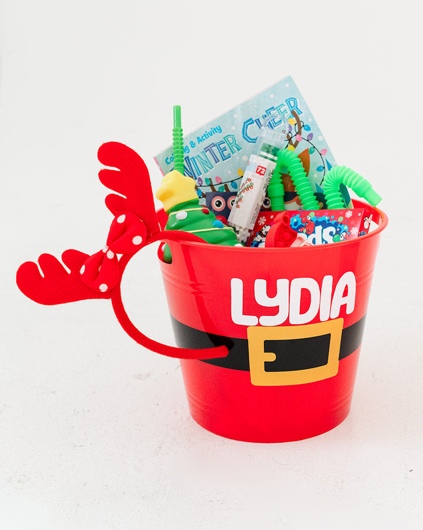 Red Christmas Santa bucket with the name Lydia on it filled with candy, Christmas party favors, activities, treats and toys on a white background.