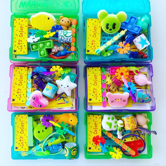 Six small, clear plastic containers with colorful lids. Each container is filled with a variety of small toys and trinkets. The containers have a label that reads 'Let's Color!' in yellow letters on a green background. The toys include a green and yellow fidget toy, a star-shaped toy, a pink cat-shaped toy, and a green and yellow frog-shaped toy.