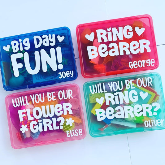 4 wedding themed busy boxes. Blue box with big day fun wording, 2 hearts and name Joey. Red box with ring bearer, 2 hearts and name George. Pink box with will you be our flower girl?, 2 flowers and name Elise. Turquoise ring bearer box name Oliver.