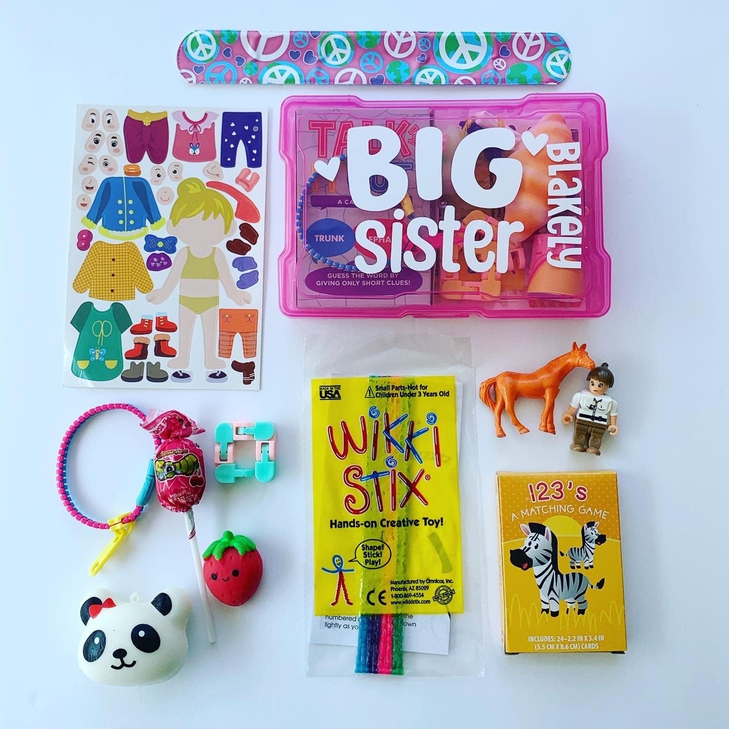Pink big sister box with name Blakely with all the activities that come inside the box surrounding it. Stickers, Wikki Stix, 1 2 3 matching game, lollipop, mini figure, squishy, fidgets, zipper bracelet, horse