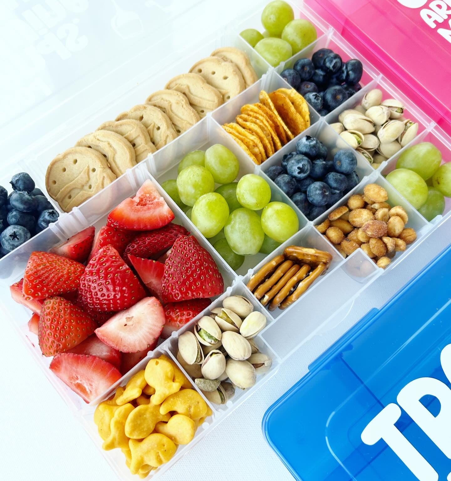 Assorted snacks including fruits, cookies, and nuts in a divided container with a blue lid.