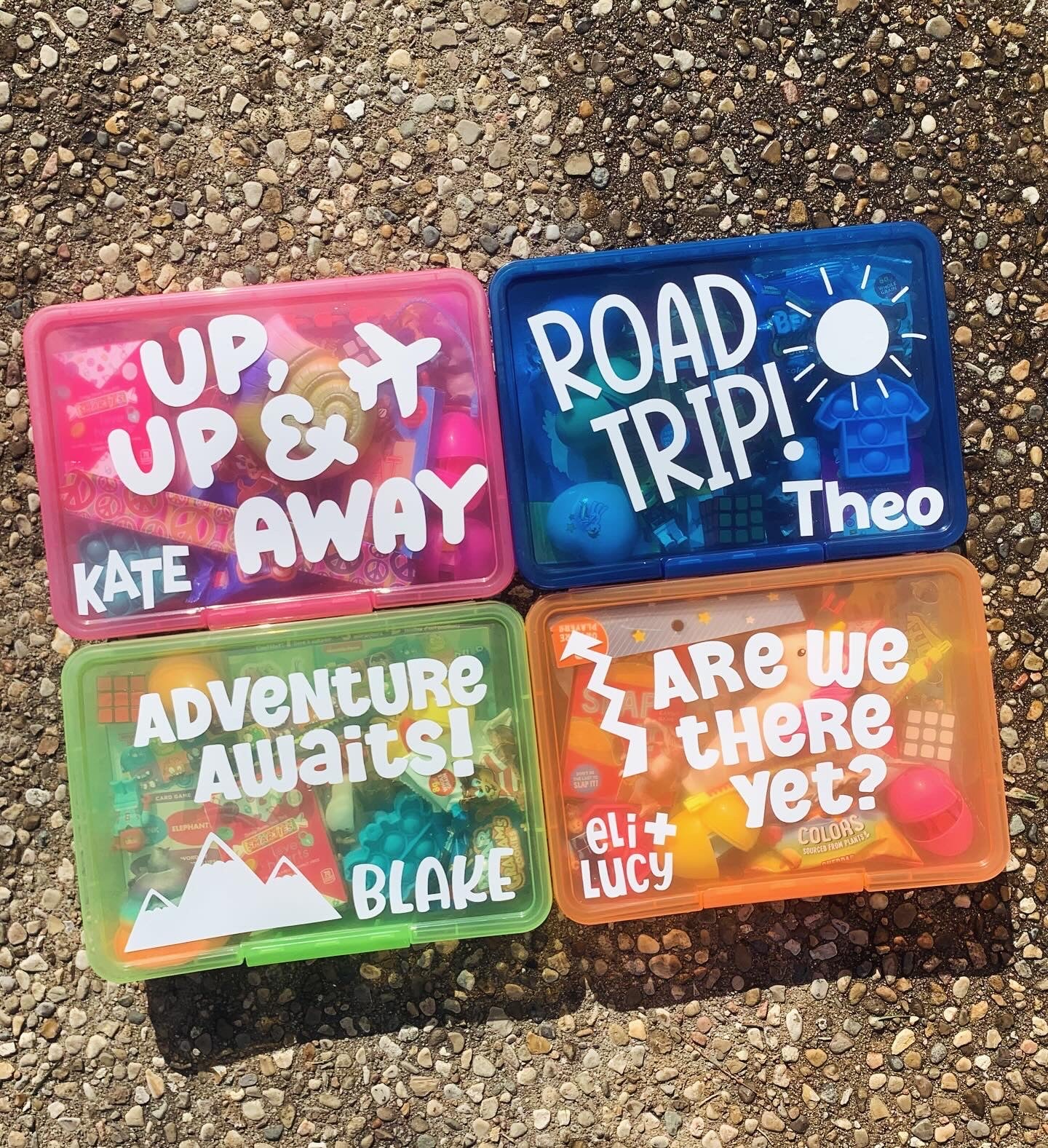 bright colored travel activity boxes - pink box with "up, up and away" with airplane, dark blue box with "road trip" and a sunshine, green box with "adventure awaits" and mountain, orange box with "are we there yet?" and arrow - all personalized with child's name