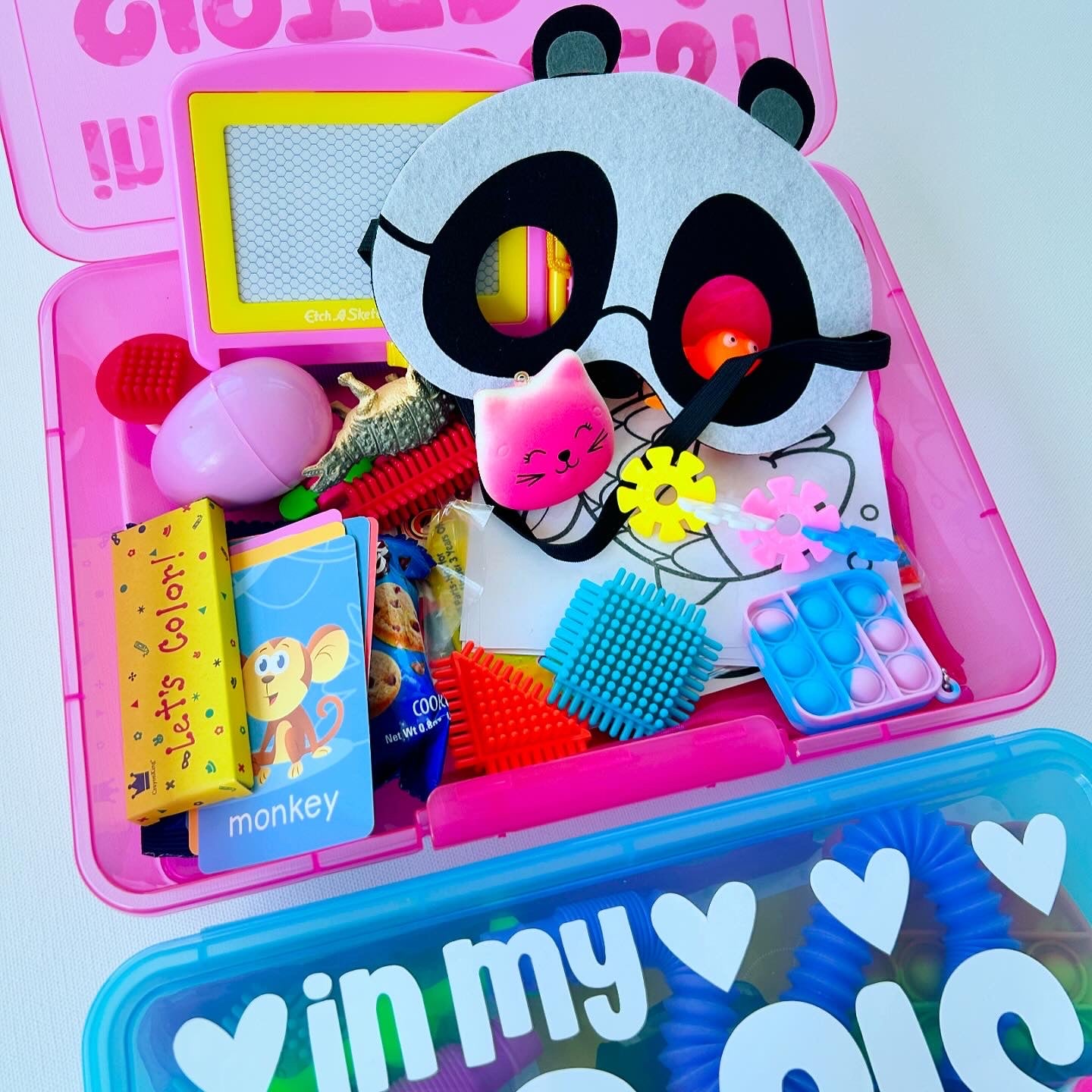 Colorful toy set with panda mask and various items in a pink container on a white background.