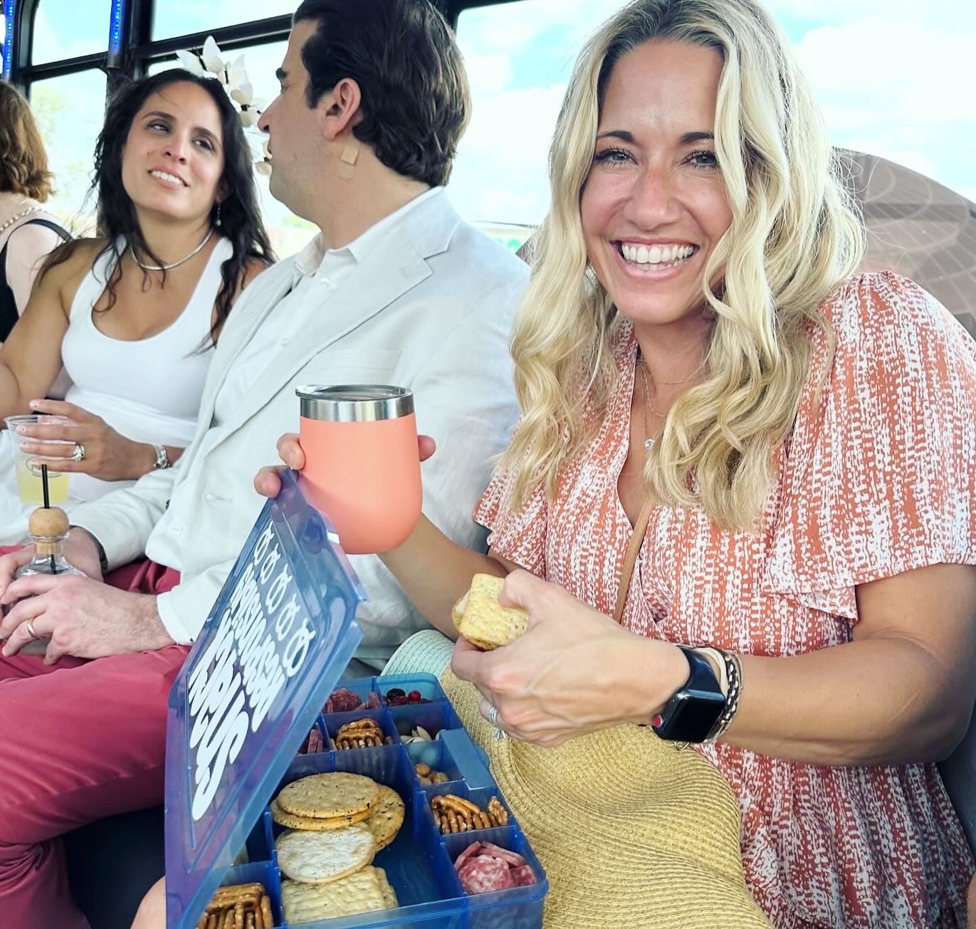 Woman holding a pink cup and a snack, with others in the background