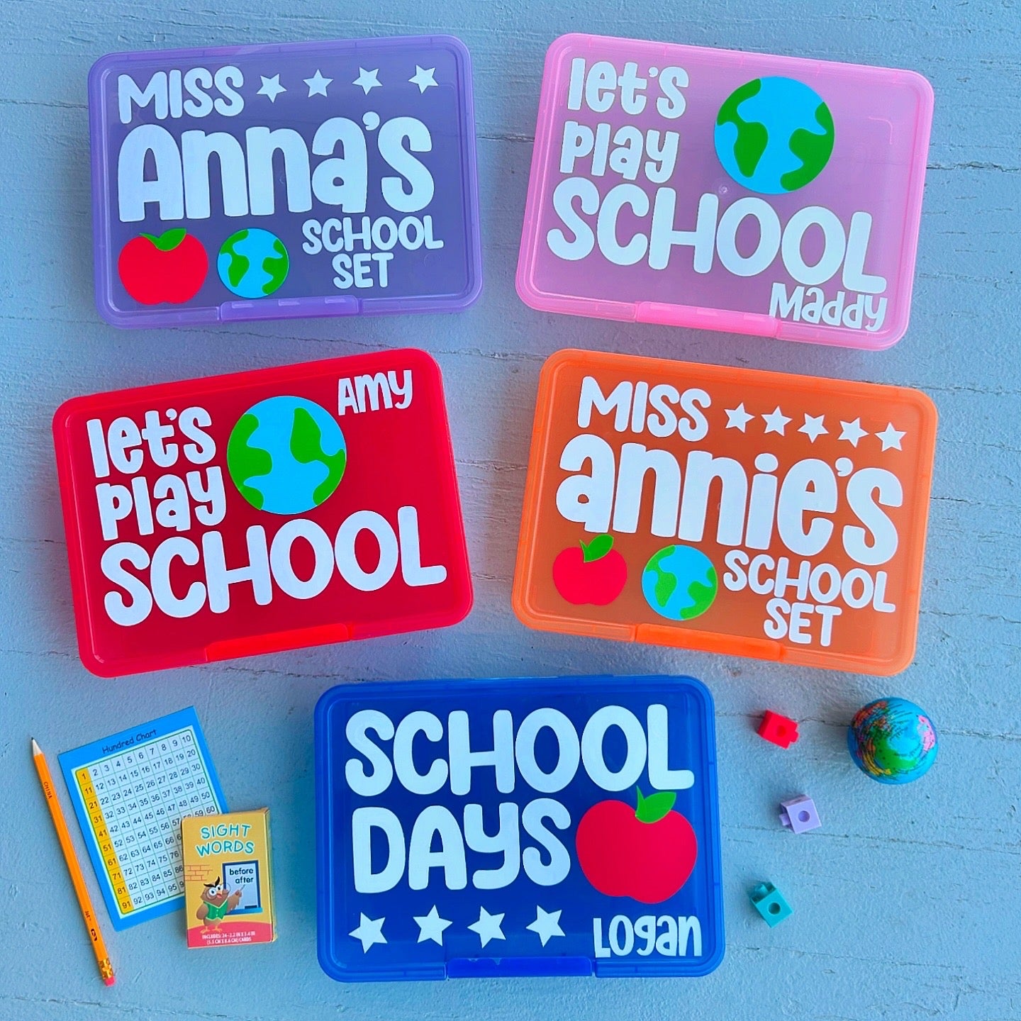 Five colorful containers with personalized names on a blue surface with educational items.