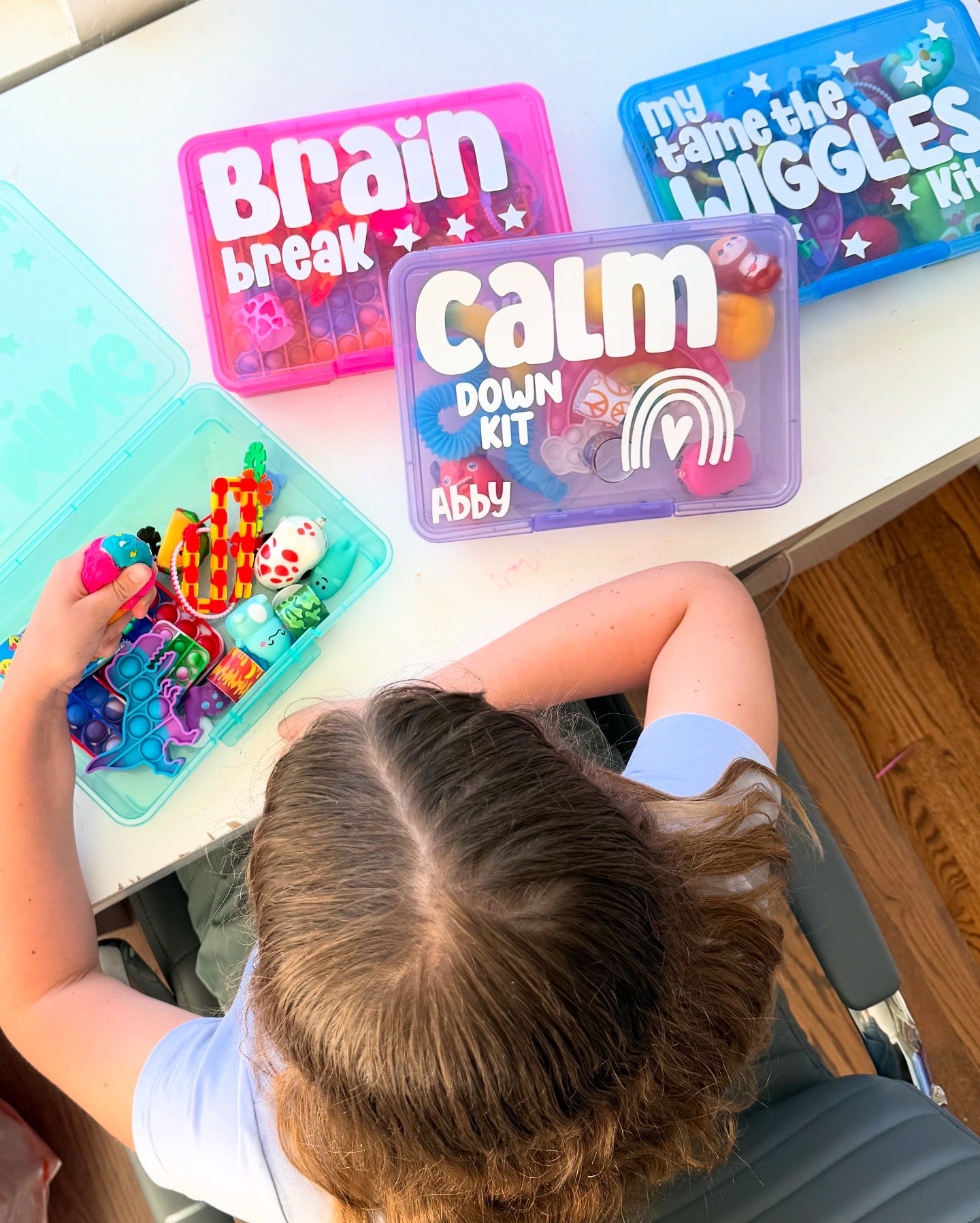 Child playing with a 'Calm Down Kit' while other kits labeled 'Brain Break' and 'My Name is Wiggles' are visible on a table.