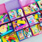 Colorful educational toys and books in a pink and purple storage box on a light gray surface.