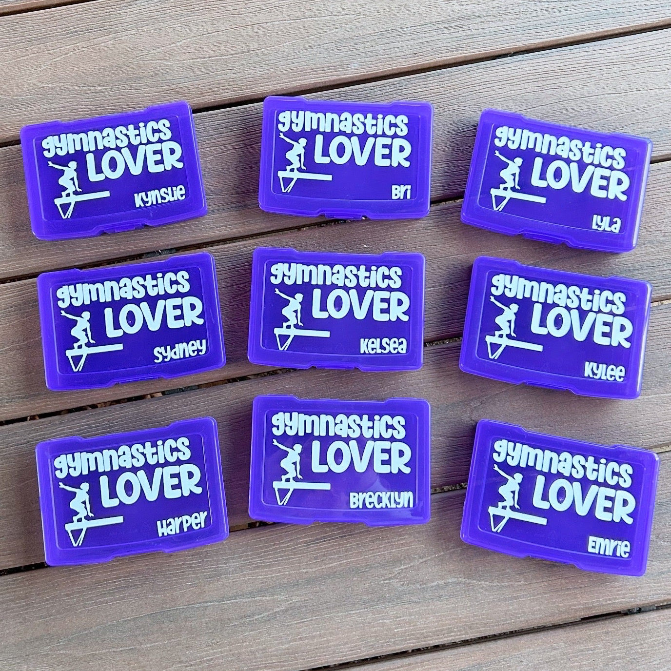 Purple 'Gymnastics Lover' patches with names on a wooden surface