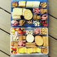 Snack box with various food items including crackers, cheese, and fruits on a wooden surface.