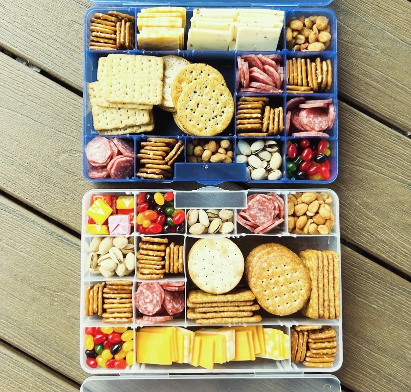 Snack box with various food items including crackers, cheese, and fruits on a wooden surface.