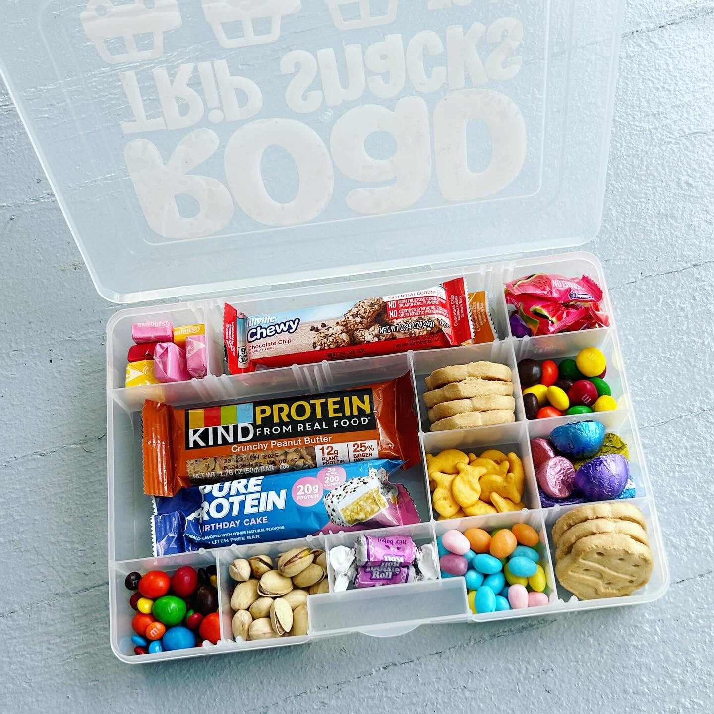 Assorted snacks in a clear plastic container on a light blue surface