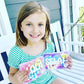 Young girl holding two clear plastic boxes with 'Lola and 'Selah' personalized on the front of the box. Each activity kit is filled with fun toys for children including a bendy snake fidget, slap bracelet, pop it fidgets and more.