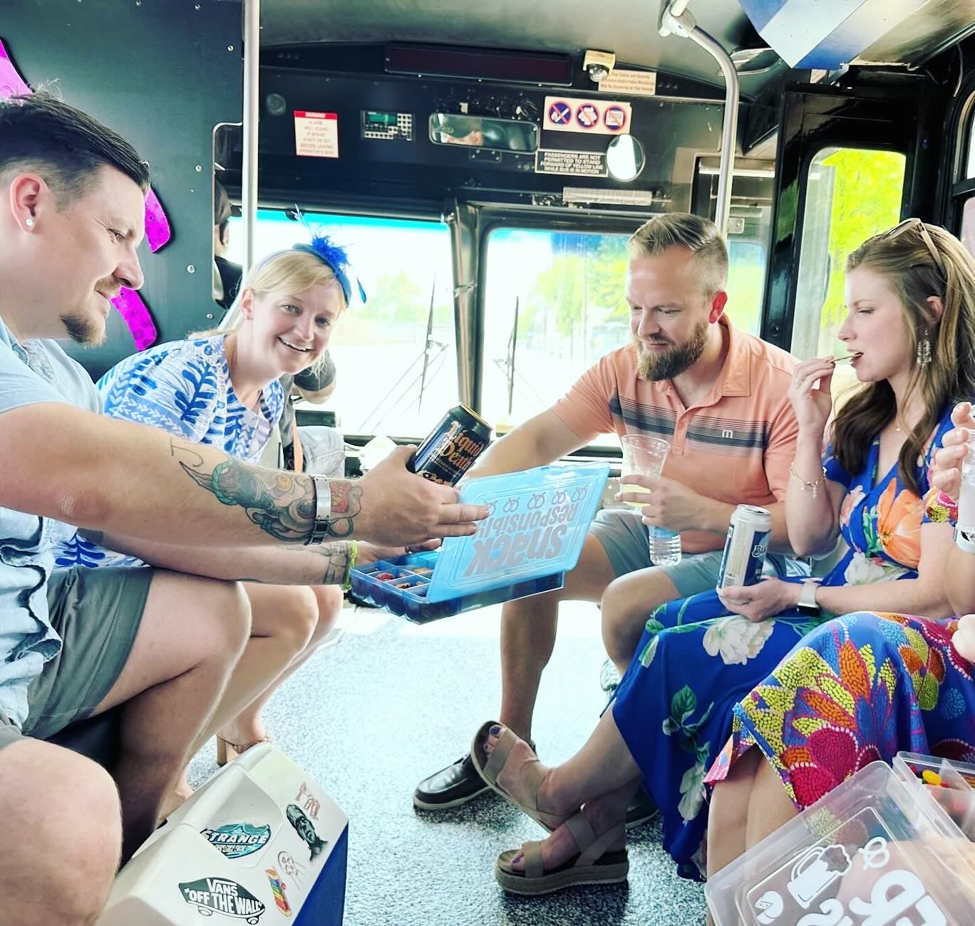 Group of people sitting inside a vehicle, possibly a bus or van, with drinks and snacks.