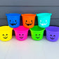 Colorful Halloween buckets with jack-o'-lantern faces against a gray wall.