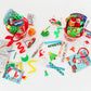 2 red Christmas buckets filled with Christmas and holiday themed goodies for kids. Surrounding the buckets are Christmas coloring books, activities, fidgets, novelty glasses and headbands, slap bracelets, stickers, cups and more.