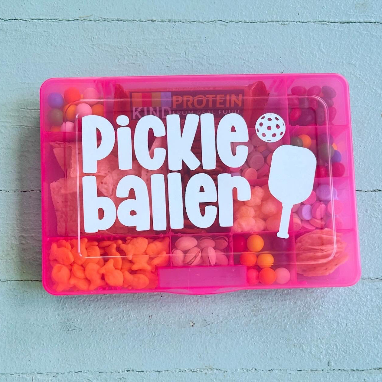 Pink container labeled 'Pickle Baller' with colorful candies on a light blue wooden surface
