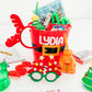 Red bucket with 'LYDIA' personalized on it, filled with children's toys and activities on a white background. Perfect for Christmas Eve or Christmas morning.