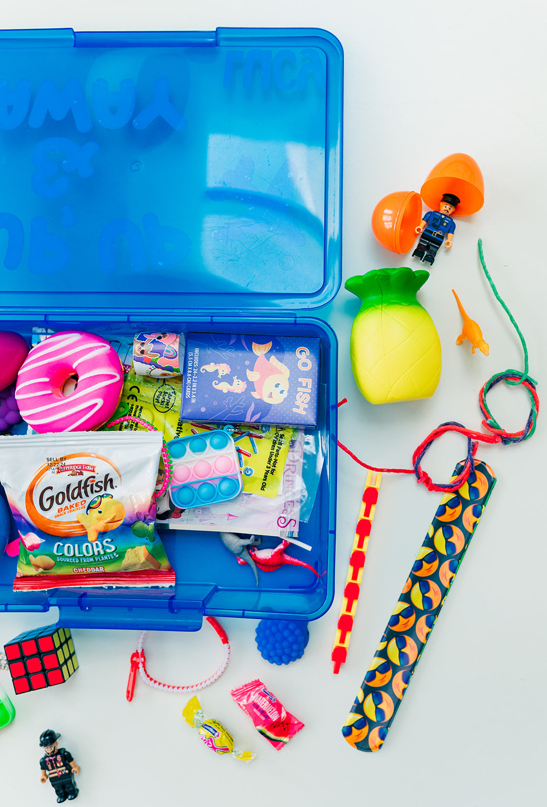 Blue tackle box with assorted items including toys and snacks on a white background