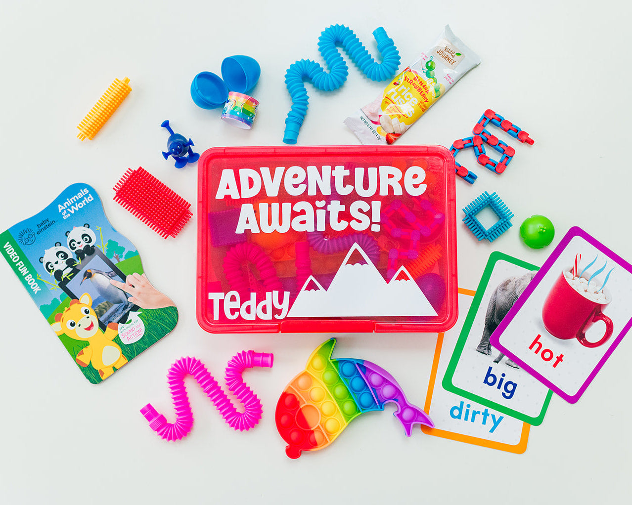 Colorful children's toys and cards with 'Adventure Awaits! Teddy' packaging on a white background