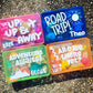 bright colored personalized travel activity boxes filled with fidgets and toys - pink box - up up and away, blue box - road trip, green box - adventure awaits, orange box-are we there yet - all personalized with child's name