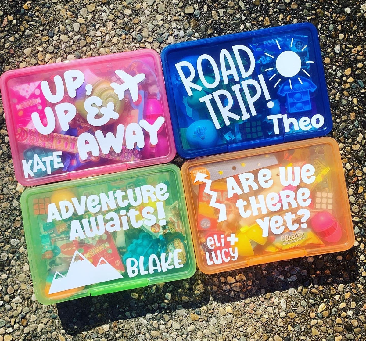 bright colored personalized travel activity boxes filled with fidgets and toys - pink box - up up and away, blue box - road trip, green box - adventure awaits, orange box-are we there yet - all personalized with child's name