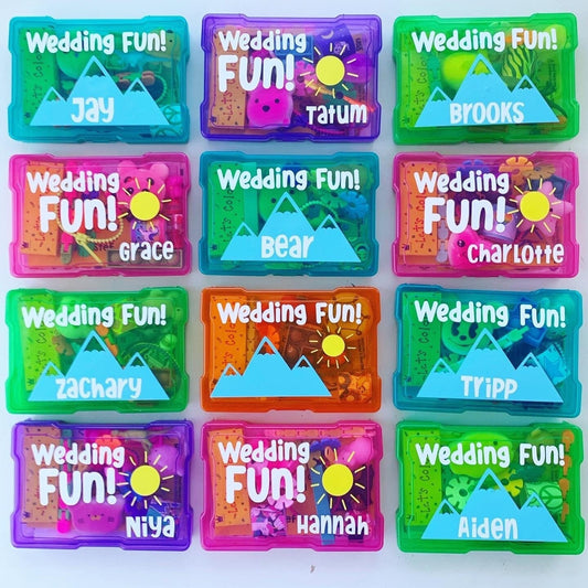 Twelve colorful plastic containers filled with wedding-themed activities for children. The containers are labeled with the words 'Wedding Fun!' and a name. Sunshine and mountain images are also on each box, making these perfect for destination weddings, beach weddings or mountain weddings. Great flower girl and ring bearer gifts.