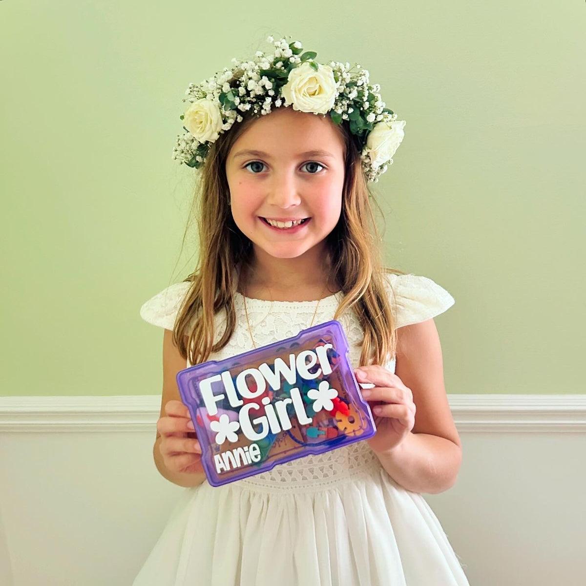 A purple plastic box with the words 'Flower *Girl* Annie' on the front. The box is filled with colorful flower petals and other decorations. Great flower girl proposal or flower girl gift idea.