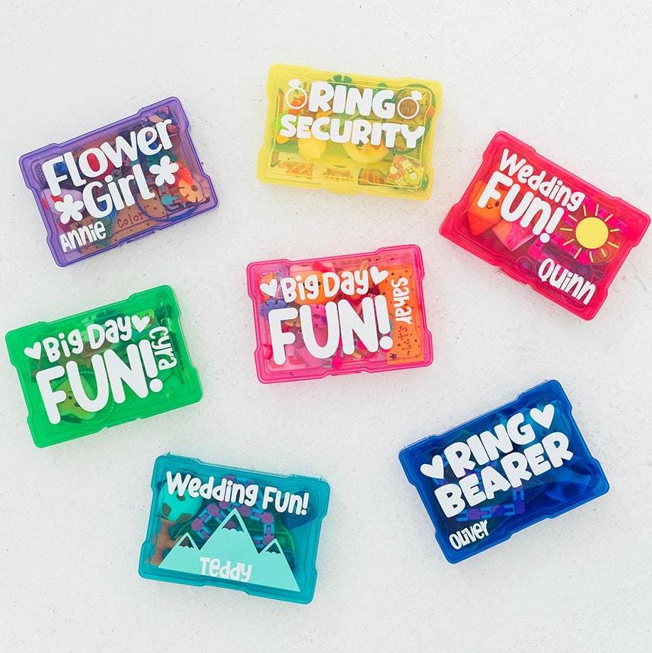 Bright and colorful wedding-themed activity kits on a white background. Various wording on each box including flower girl, ring security, wedding fun, big day fun and ring bearer. Each box is filled with trinkets, activities and wedding coloring pages to entertain children at a wedding.