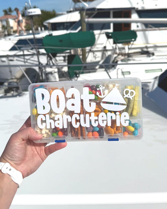 May include: A clear plastic container with a white label that reads &#39;Boat Charcuterie&#39;. The container is filled with various snacks, including pretzels, popcorn, and candy. The container has a blue latch.